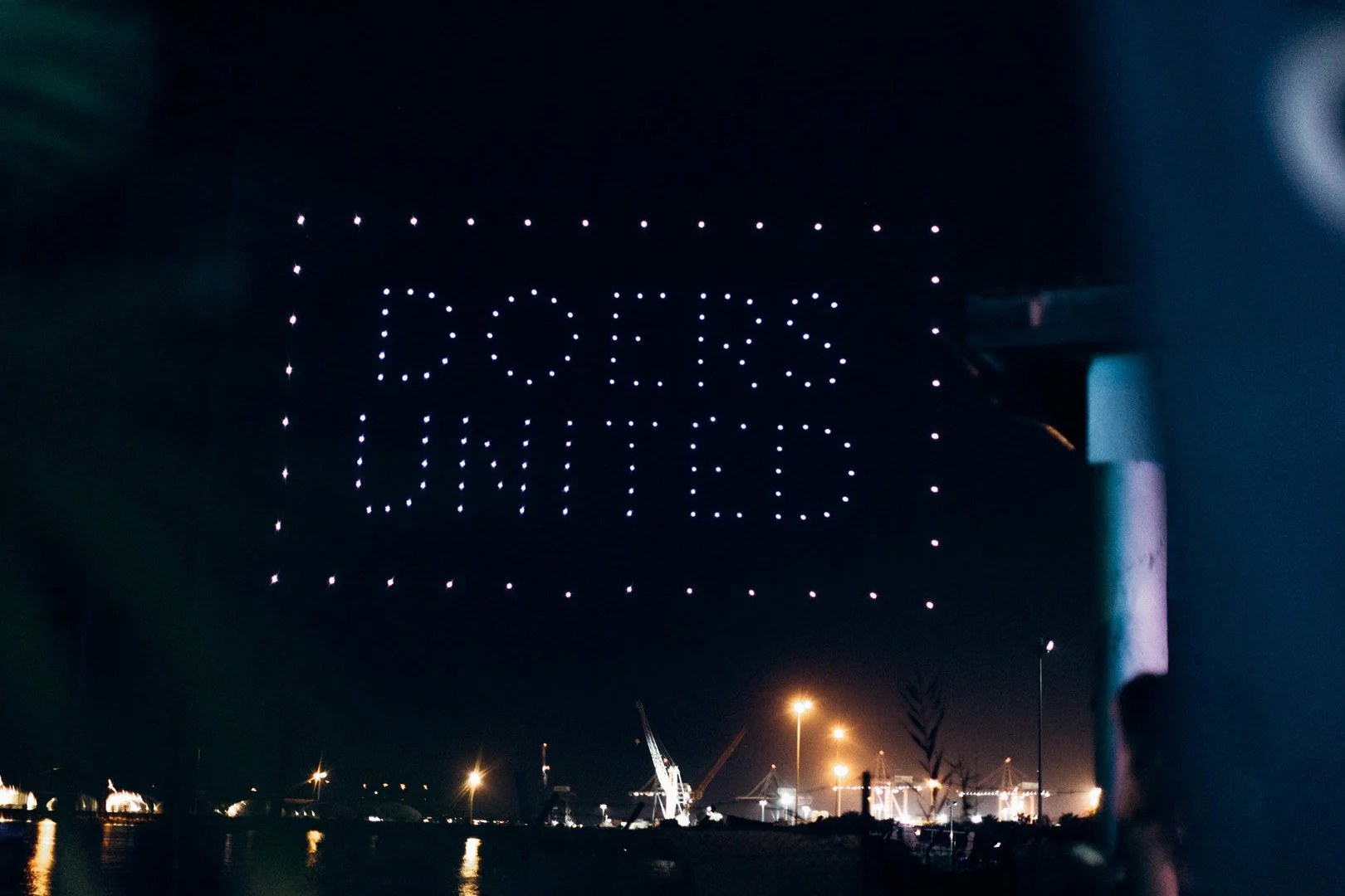 A drone show spelling out Doers United over the water at night