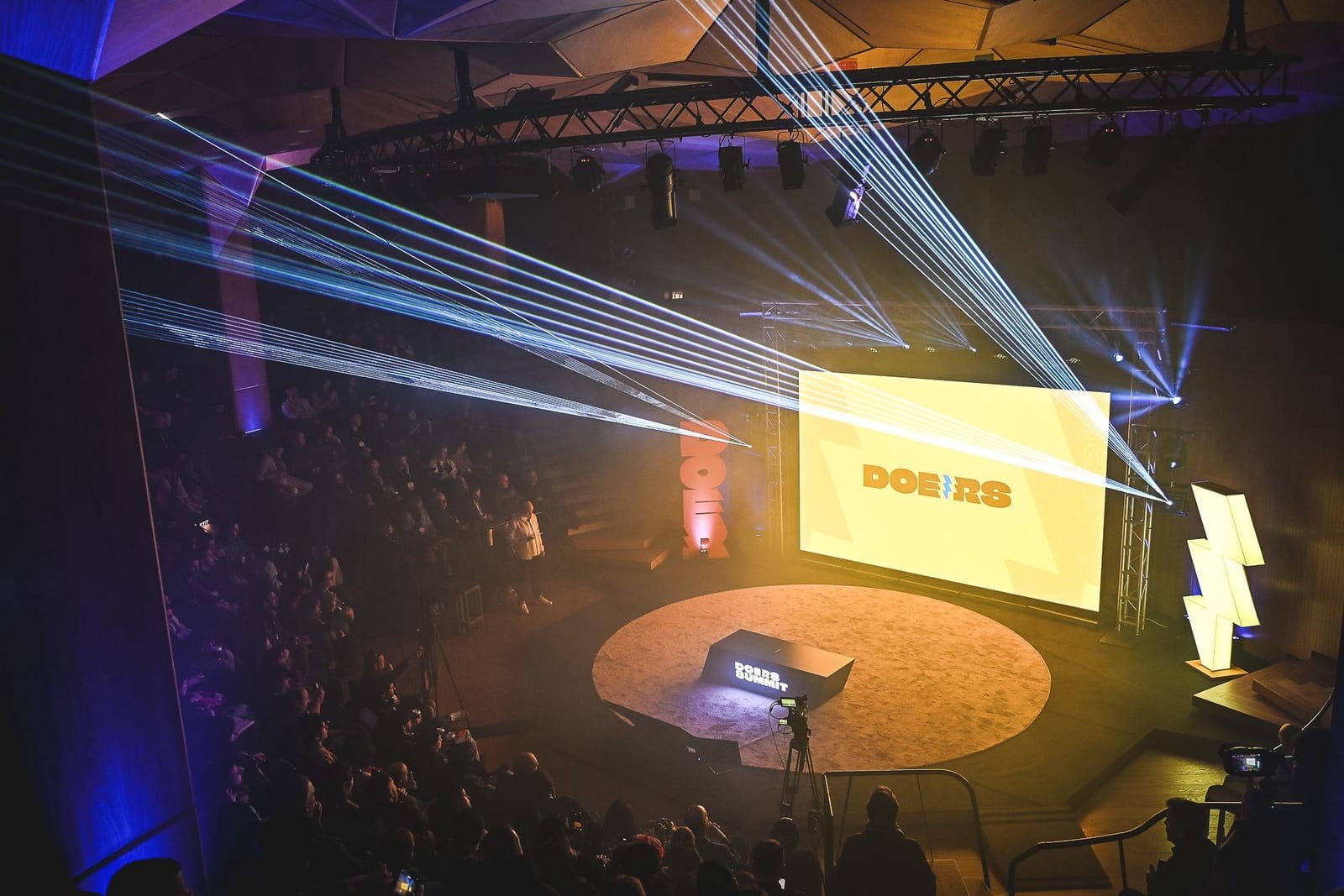 A packed amphitheatre under laser light at Doers Summit