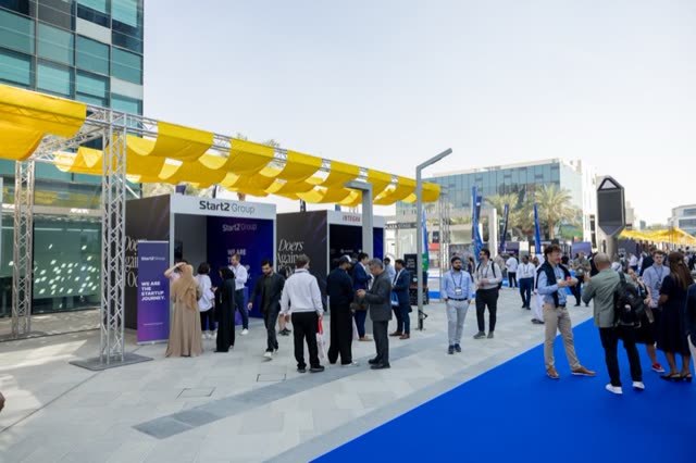A daylight expo boulevard in Dubai, attendees between exhibitor stands