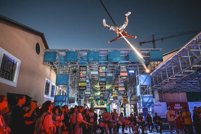 An aerial performer above a red-lit outdoor crowd